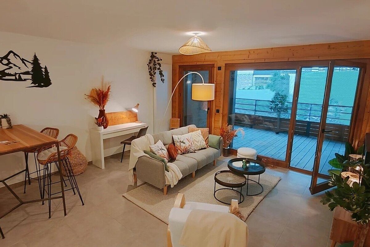 A cozy, modern living space with a sofa, dining area, desk, and large glass doors opening to a deck, featuring warm wood accents and rustic decor.