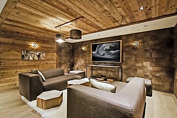 A rustic media room featuring wood-paneled walls and ceiling, modern gray sofas, a large TV, and accent lighting.