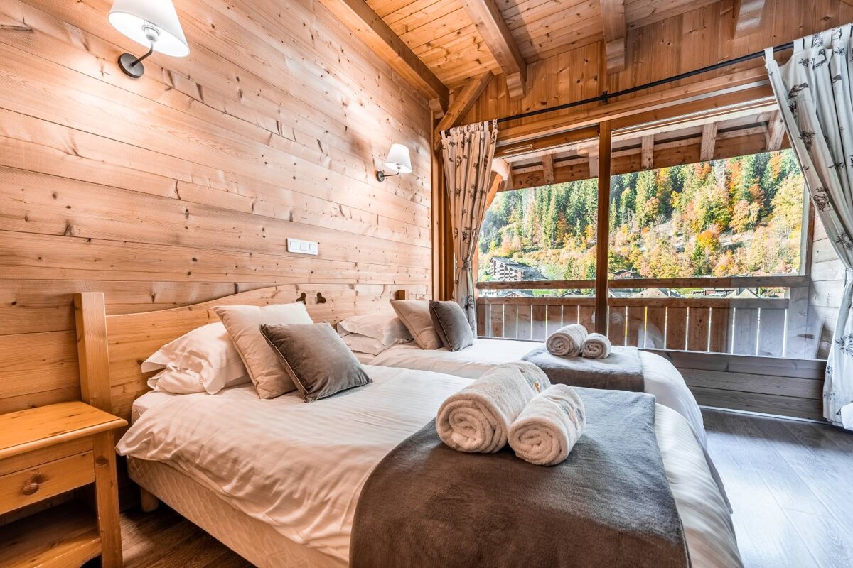 A bedroom with two beds and a balcony overlooking a forest
