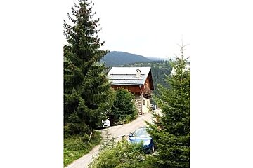 A blue car is parked in front of a wooden house in the mountains