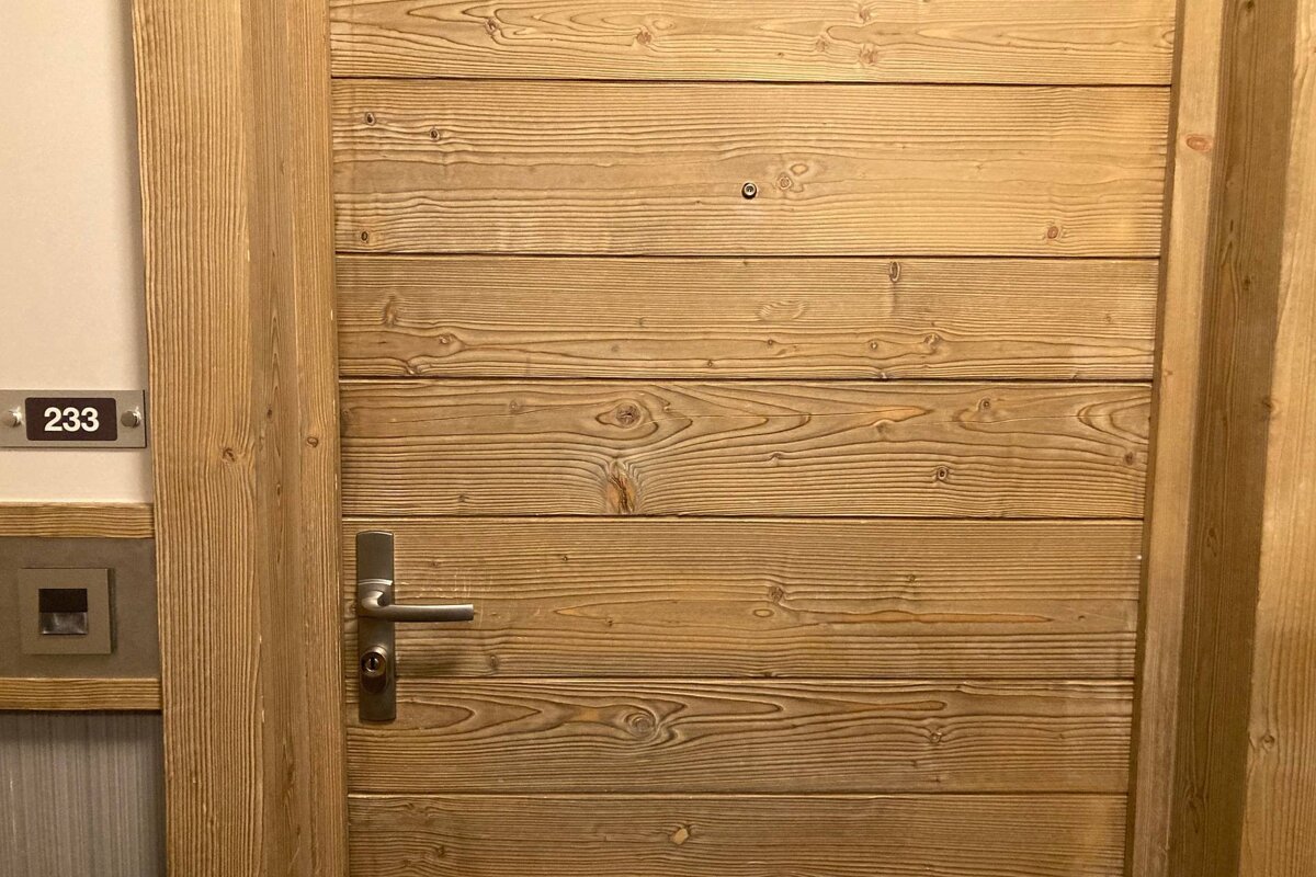 A wooden door with horizontal planks and a metal handle, featuring room number 233 on the wall beside it.