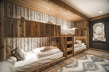Rustic wooden bunk beds with tree-patterned wallpaper, a patterned rug, and a bear painting in a cozy cabin-style bedroom.