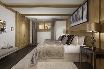 A stylish and cozy bedroom with wood paneling, a large bed covered in a faux fur throw, dark floors, and a picture window.