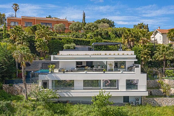 A large white house sits on top of a hill surrounded by palm trees
