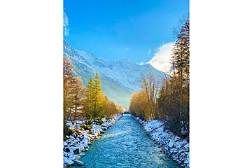 A river runs through a snowy forest with mountains in the background