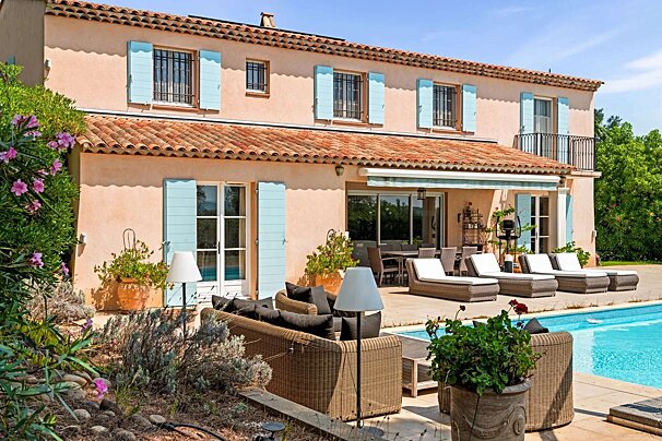 A sunny peach villa with blue shutters, a terracotta roof, and a sparkling pool. It features inviting outdoor lounge and dining areas.
