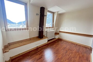 Empty room with hardwood floor, white walls, and mountain views from two windows. Features wooden sills, a radiator, and an exposed beam.