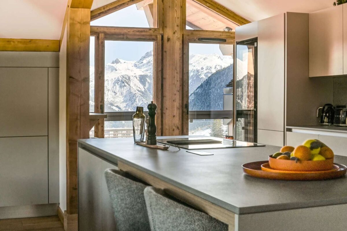A kitchen with mountains in the background and a bowl of fruit on the counter
