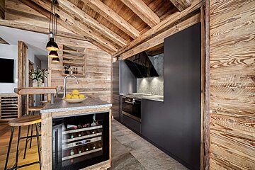 A rustic wooden chalet kitchen features modern dark cabinetry, an island with a sink and wine cooler, and stylish pendant lighting.
