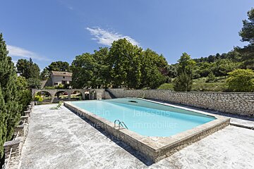 A large swimming pool is surrounded by a stone wall with the words made in lanssens immobilier written on it