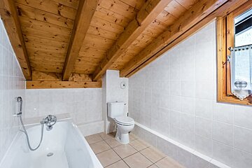 Rustic attic bathroom featuring a slanted wooden ceiling, white tiled walls, a bathtub, and a toilet.
