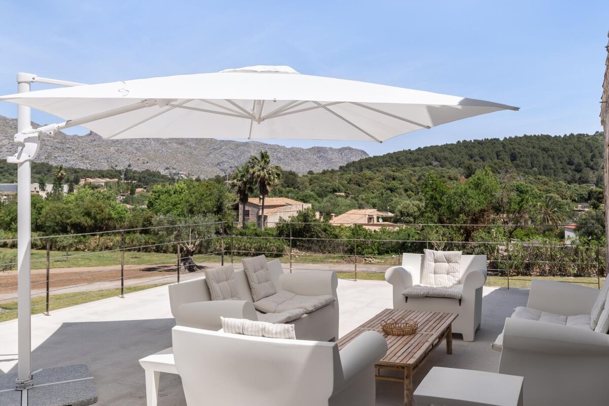 A white umbrella sits over a patio with white furniture