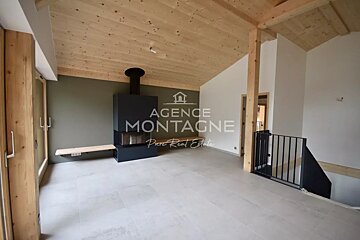 Spacious room with a sloped wooden ceiling, modern black fireplace, light floor tiles, green/white walls, wood accents, and a black stair railing.