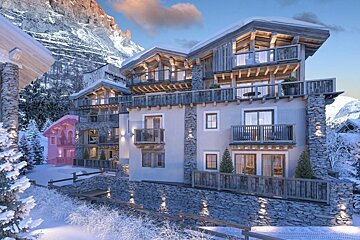 A serene winter mountain village with luxurious chalet-style buildings adorned with snow, set against majestic peaks under a partly cloudy sky.