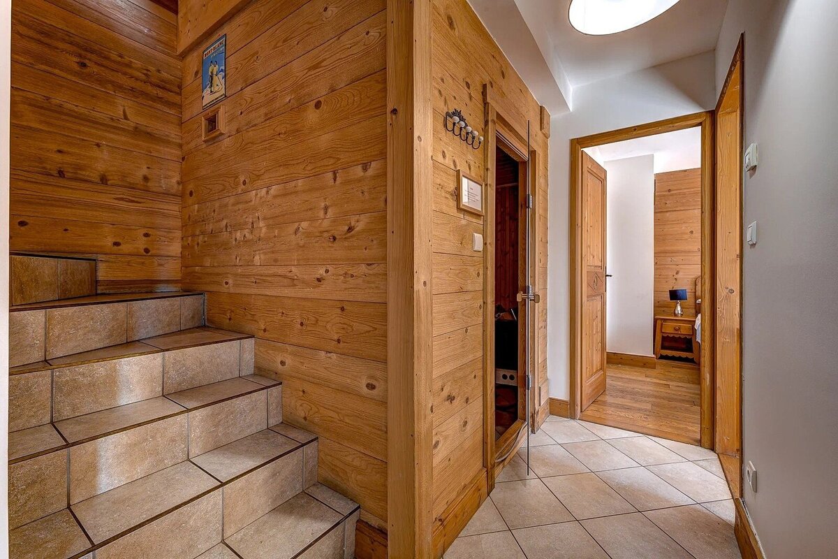 A cozy, wood-paneled interior with tiled stairs, a hallway, a small sauna-like door, and a ski-themed poster on the wall.