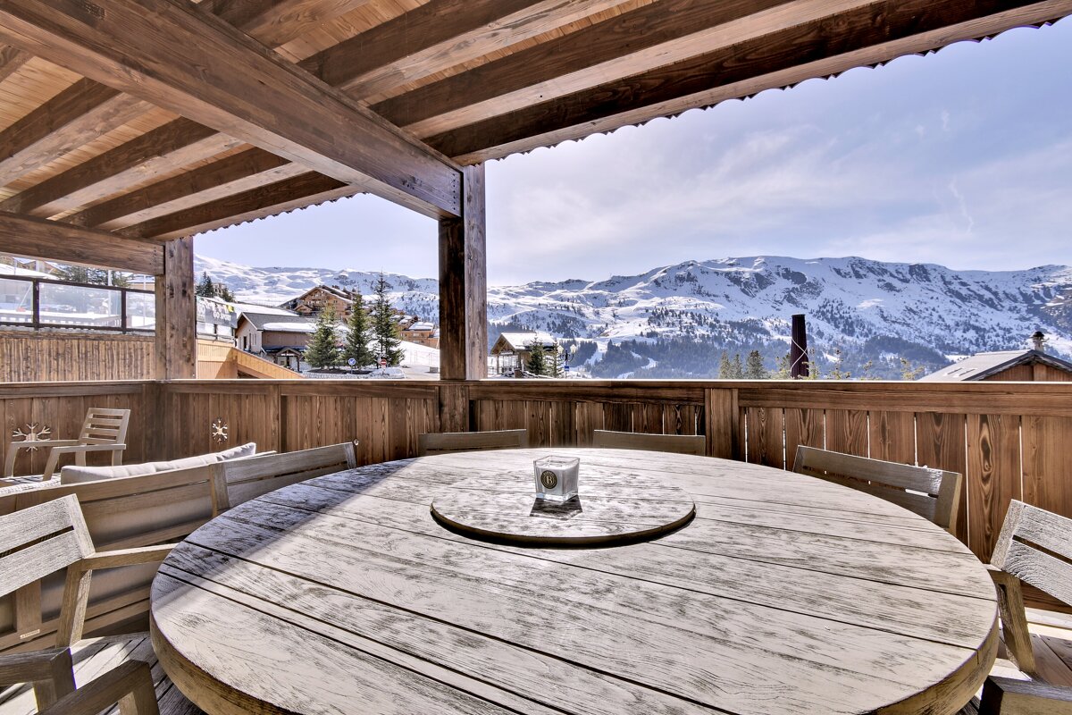 A round wooden table with a glass on it and mountains in the background