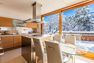 Modern kitchen and dining area featuring floor-to-ceiling windows with a snowy winter forest view.