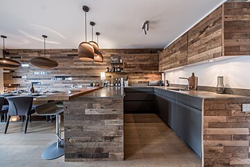 A modern kitchen and dining area featuring extensive reclaimed wood paneling, dark grey cabinets, and stylish pendant lighting.