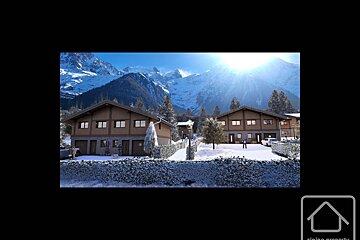Two modern chalets in a snowy mountain landscape, with frosted hedges and trees under a bright winter sun. Majestic peaks visible in the background.