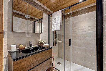 A modern bathroom features a wooden ceiling, a vanity with a black sink, and a sleek glass shower, all in warm, earthy tones.