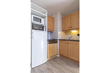 A compact kitchen with light wood cabinets, a white fridge, microwave, and oven stack, a sink, and tiled backsplash.