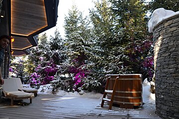 A wooden tub is surrounded by snow covered trees