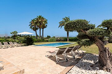 A patio with chairs and an umbrella in front of a swimming pool