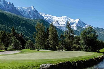 A green golf course with mountains in the background