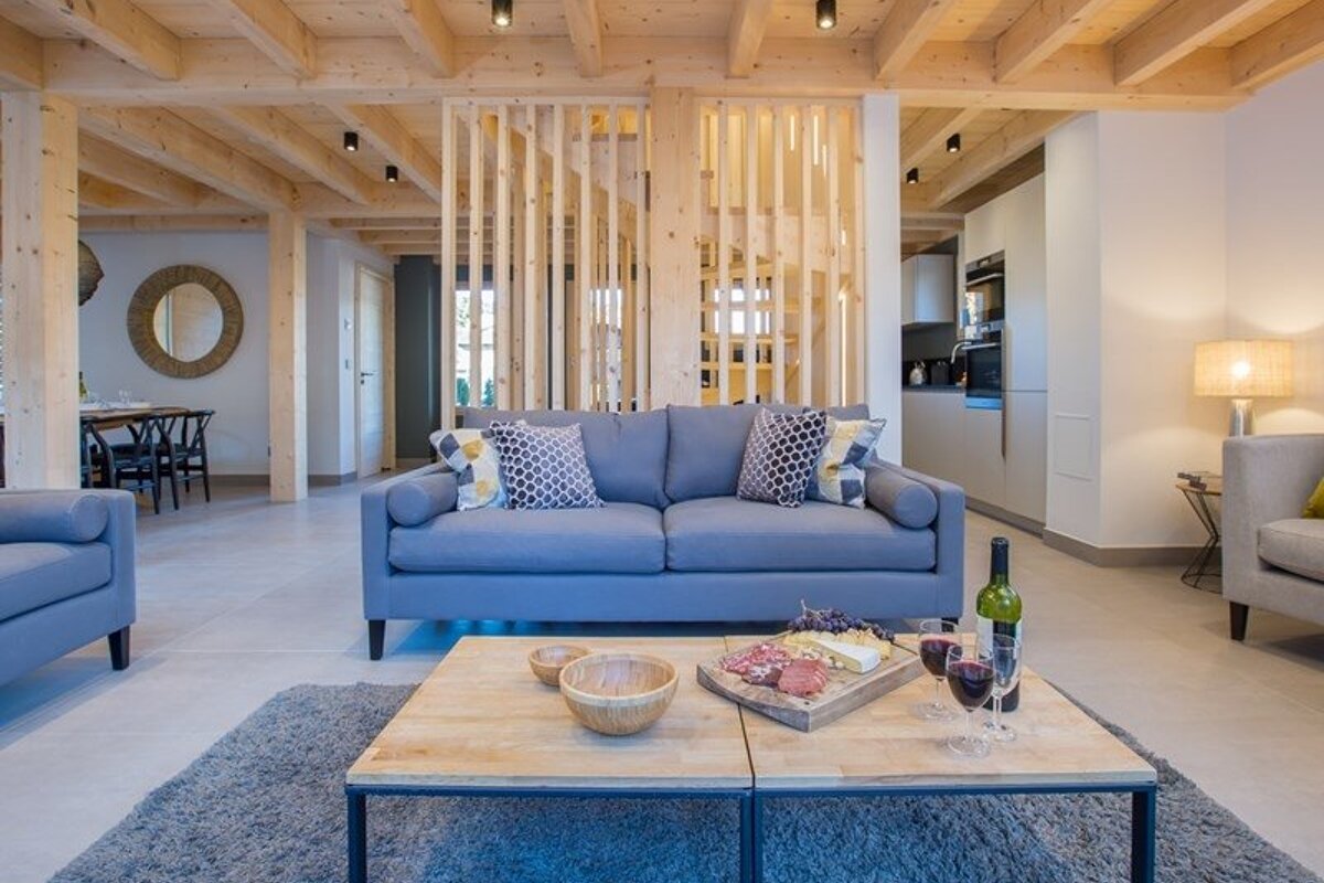 Modern living room featuring a blue sofa, exposed wooden beams, and a coffee table with wine and a charcuterie board.