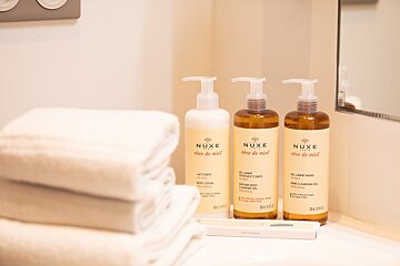 Three bottles of nuxe creme de miel are on a bathroom counter