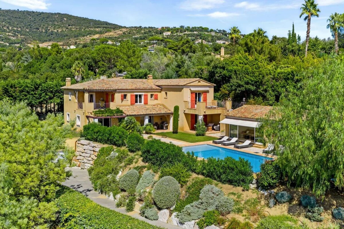 Stunning ochre villa with red shutters, a private swimming pool, and lush Mediterranean gardens cascading down a verdant hillside.