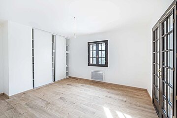 Bright, empty room with white walls, light wood floor, built-in closet, dark window, and French doors.