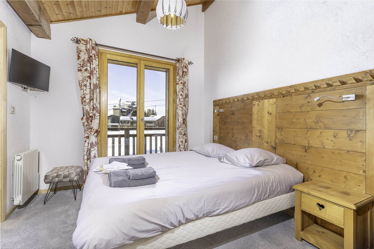 Cozy chalet bedroom with a wooden headboard, a double bed, and glass doors opening to a snowy balcony.