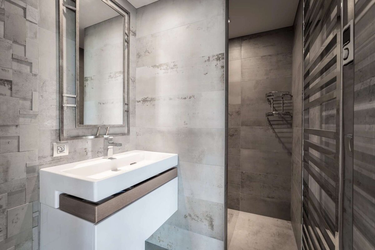 Modern gray bathroom with a white floating sink, a framed mirror, and a walk-in shower. Textured concrete-look tiles give an industrial feel.