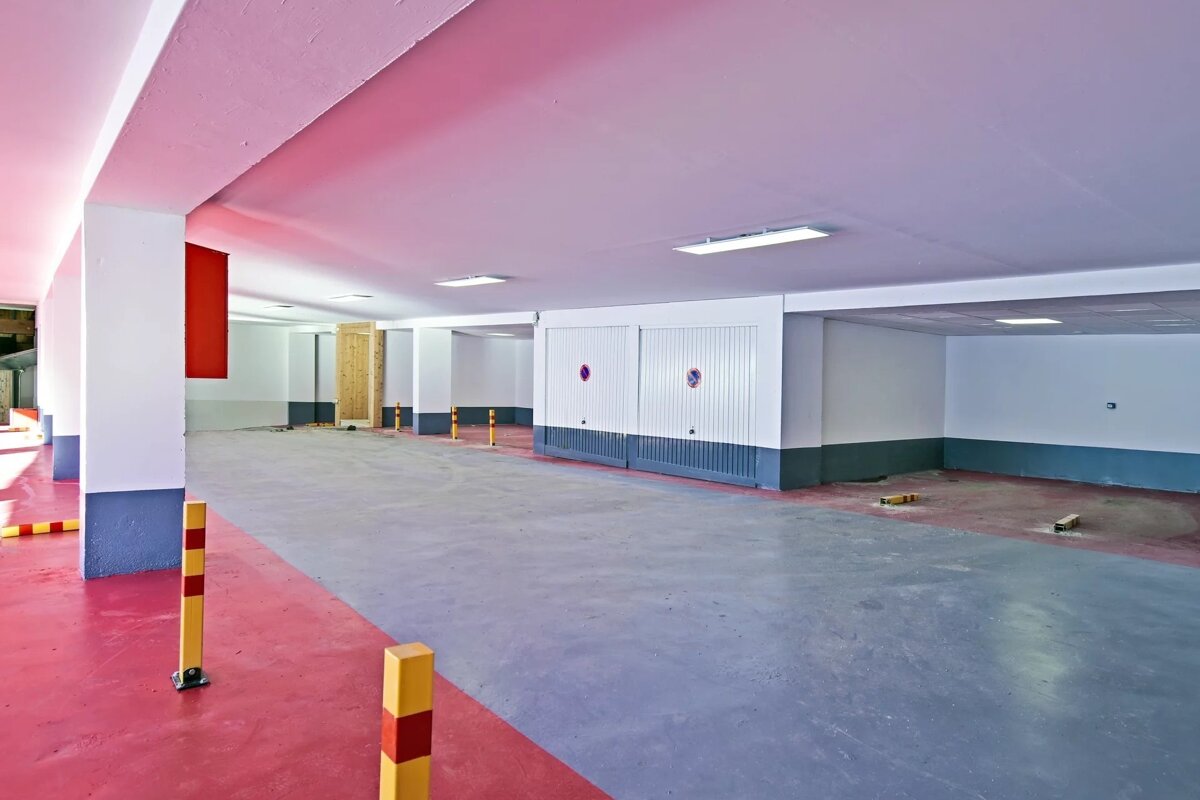 Empty indoor parking garage with a pink and grey painted floor, white support pillars, and closed garage doors.