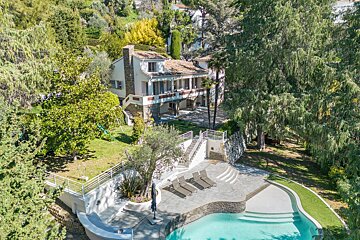 Aerial view of a luxury villa with a swimming pool, sun loungers, and lush green gardens.