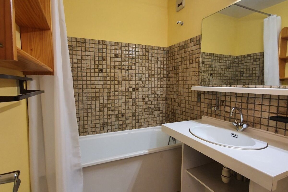 Bathroom with a white bathtub, vanity sink, yellow walls, and brown mosaic tiles.