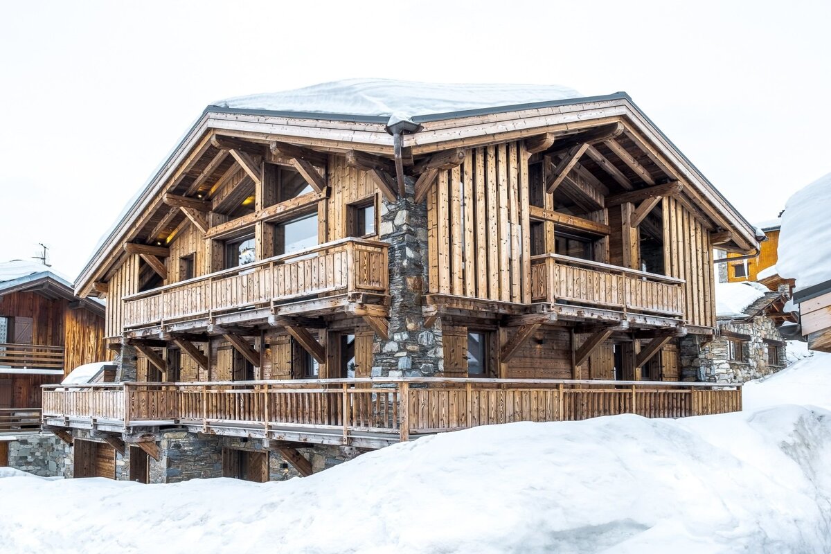 A rustic multi-level wooden and stone chalet surrounded by deep snow in a winter landscape.