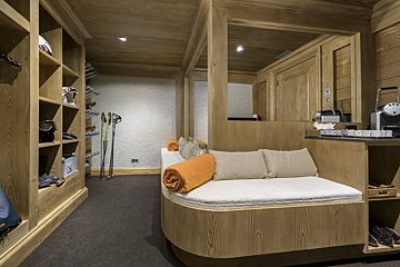 A cozy, wood-paneled ski room with built-in storage for gear like helmets and poles, a comfortable daybed, and a small coffee station.