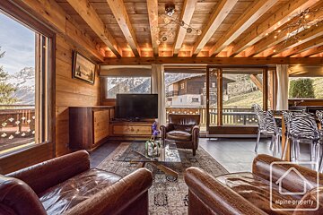 Warm, wood-paneled chalet living room with stunning mountain views. Features cozy leather seating, TV, and a dining area with unique zebra chairs.