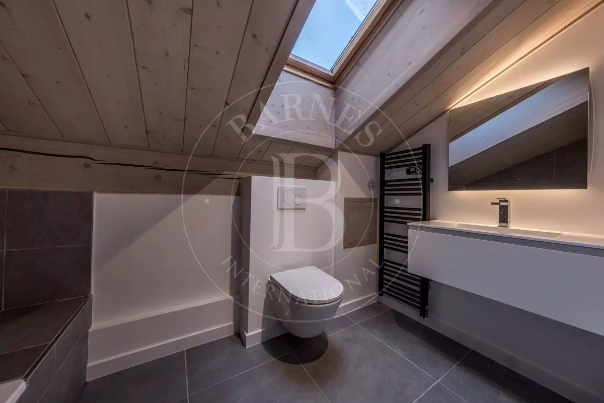 Modern attic bathroom featuring a wooden ceiling, skylight, modern toilet, vanity with backlit mirror, and a heated towel rail.