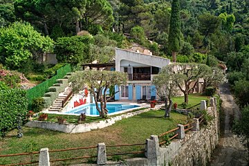 A hillside villa with a swimming pool, lawn, and trees, nestled in a lush green forest.