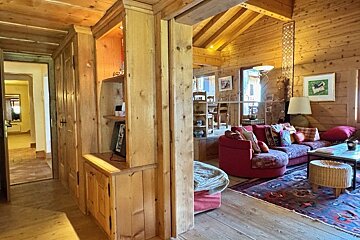 Cozy wooden cabin interior with built-in cabinets in the hallway and a warm living room featuring a red sectional sofa.