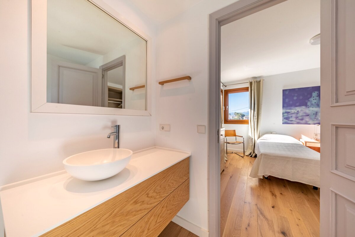 A bathroom with a sink and a mirror leading to a bedroom