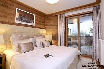 Cozy chalet bedroom with wood paneling, a large bed with neutral-toned pillows, and glass doors opening to a balcony.