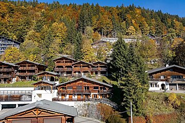 A mountainside village with rustic wooden chalets nestled among vibrant autumn trees under a clear blue sky.