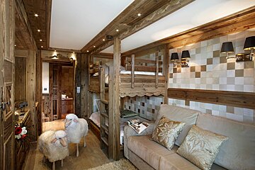 Cozy, rustic wooden chalet room with bunk beds, a comfortable sofa, and two adorable sheep figures on the floor.