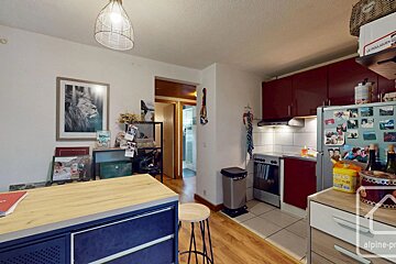 A cozy kitchen featuring red cabinets, a refrigerator, and a blue kitchen island with a wooden stool.