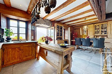A warm, rustic kitchen and dining area features exposed wooden beams, cabinetry, and walls. A large wooden workbench acts as an island, with a dining table and black chairs, and a red refrigerator. Br