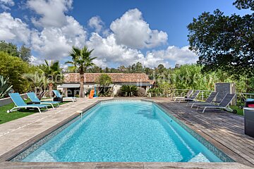 A large swimming pool is surrounded by lounge chairs and a wooden deck
